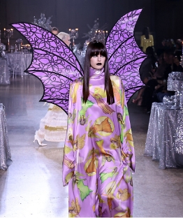 Model walking down runway with pink dress with wings